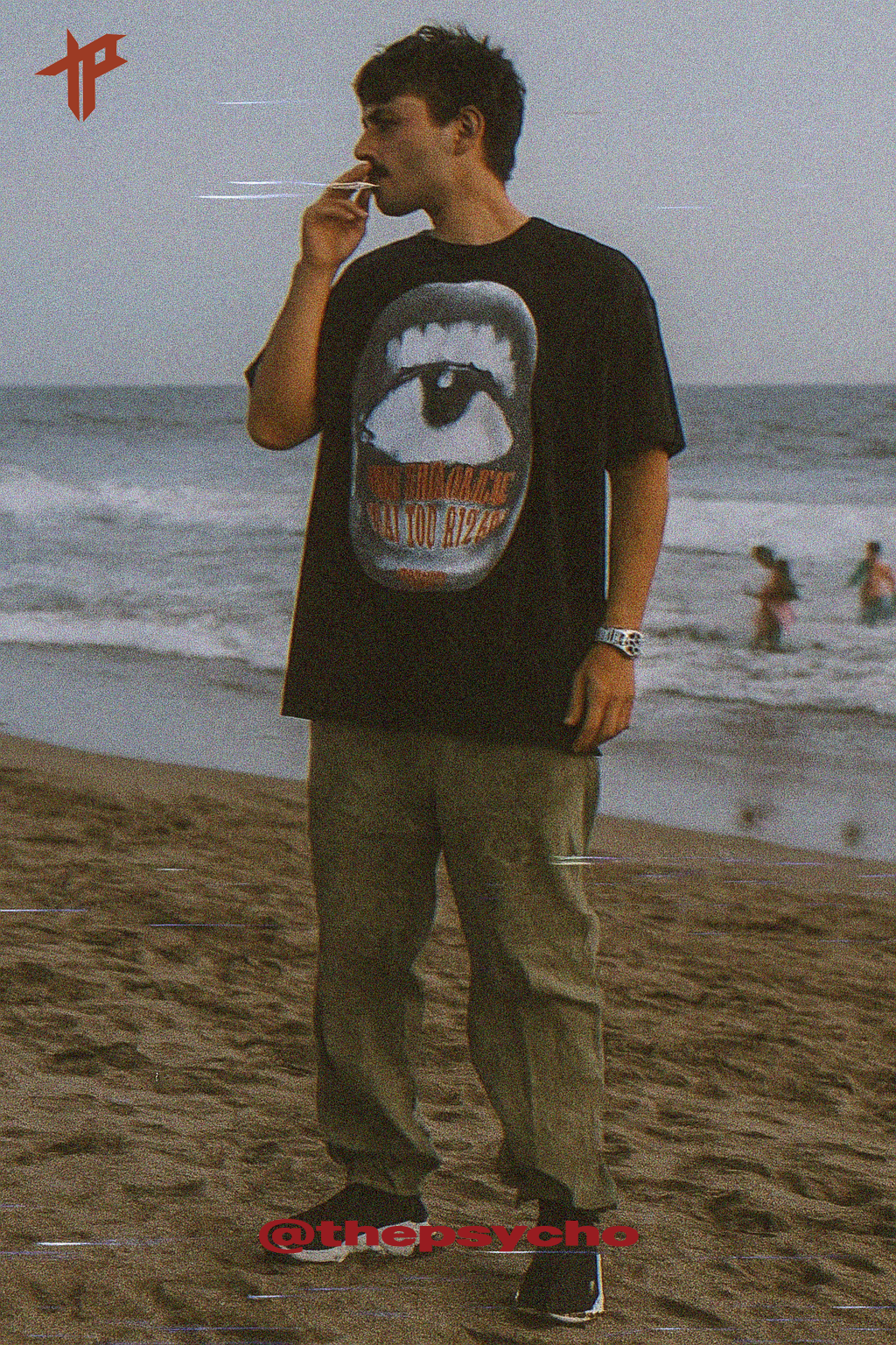 Man smoking on a beach wearing a black t-shirt with a graphic design.