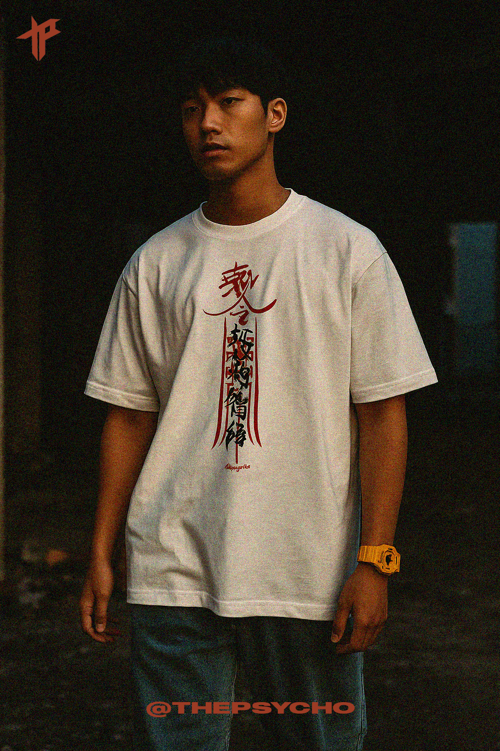 Person wearing a white t-shirt with red and black designs, standing against a dark background.